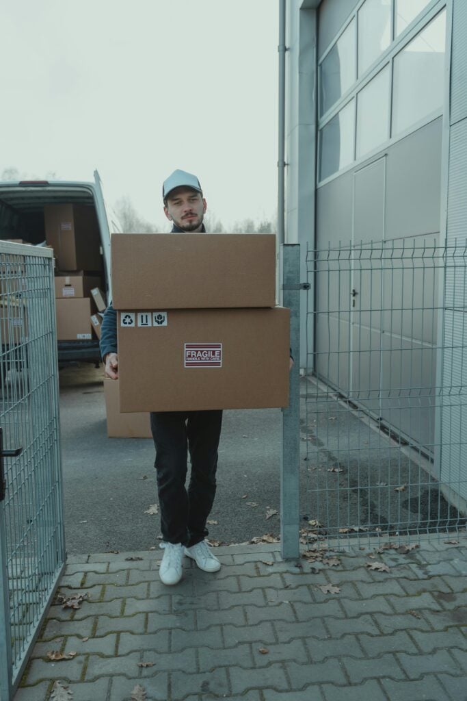 pexels-photo-6169176-6169176 Man delivering cardboard boxes in an outdoor setting wearing casual attire.