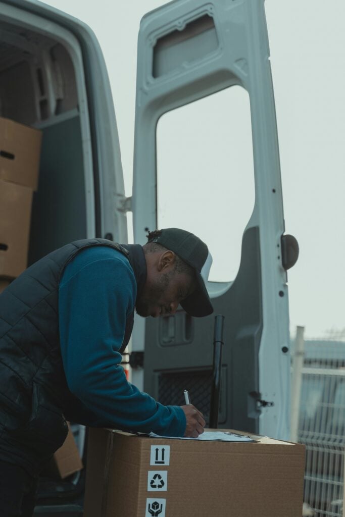 pexels-photo-6169191-6169191 A delivery worker signs documents outside a parked van, managing logistics efficiently.