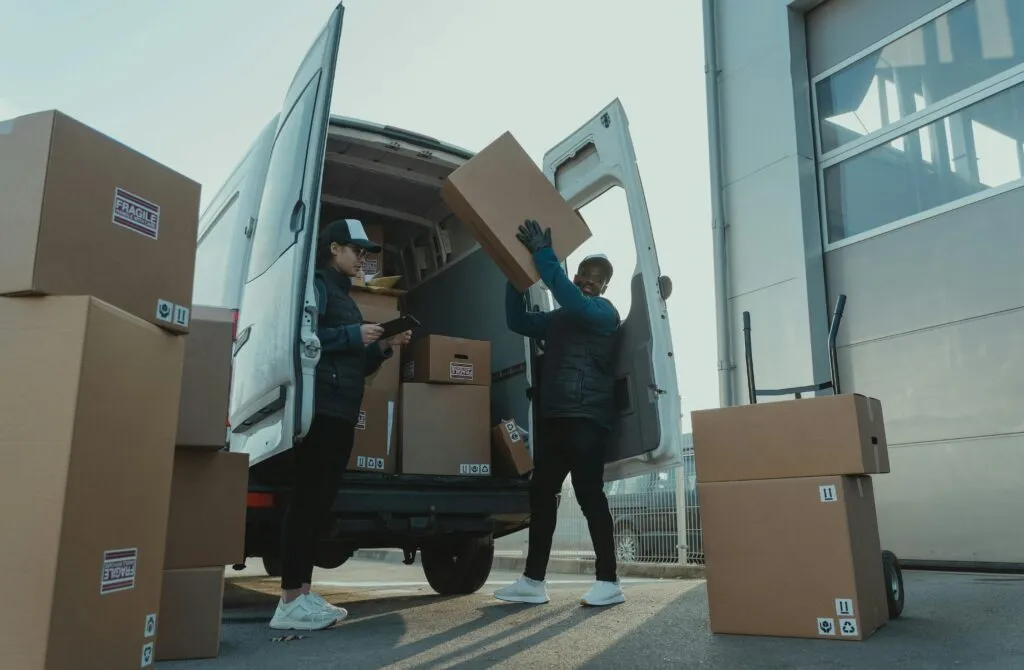 pexels-photo-6169670-6169670 Workers loading boxes into a delivery van at a warehouse facility outdoors.