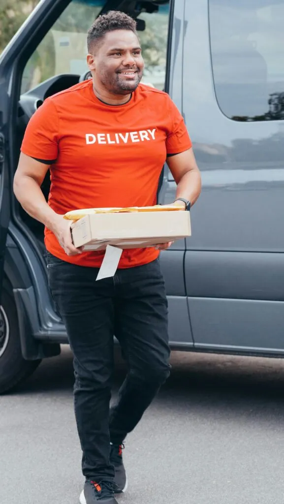pexels-photo-6868170-6868170 Smiling courier delivering a package from a van, showcasing reliable delivery service.